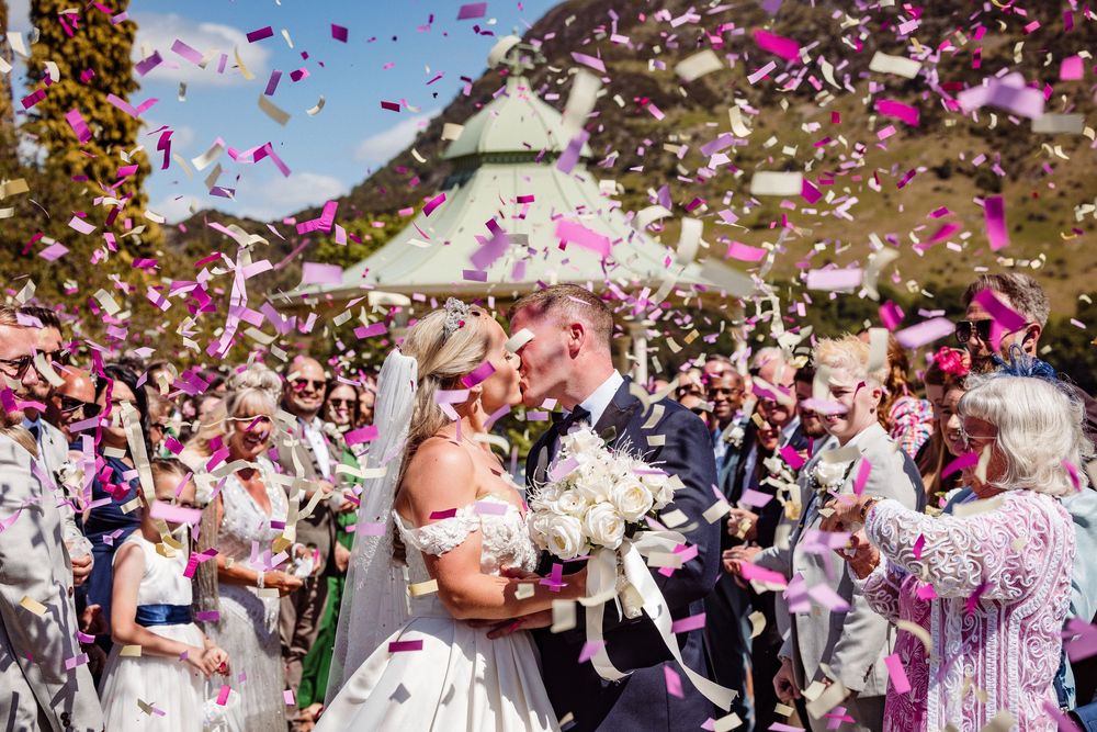 Wedding guests shower the newlyweds with pink flower petals during an outdoor celebration.