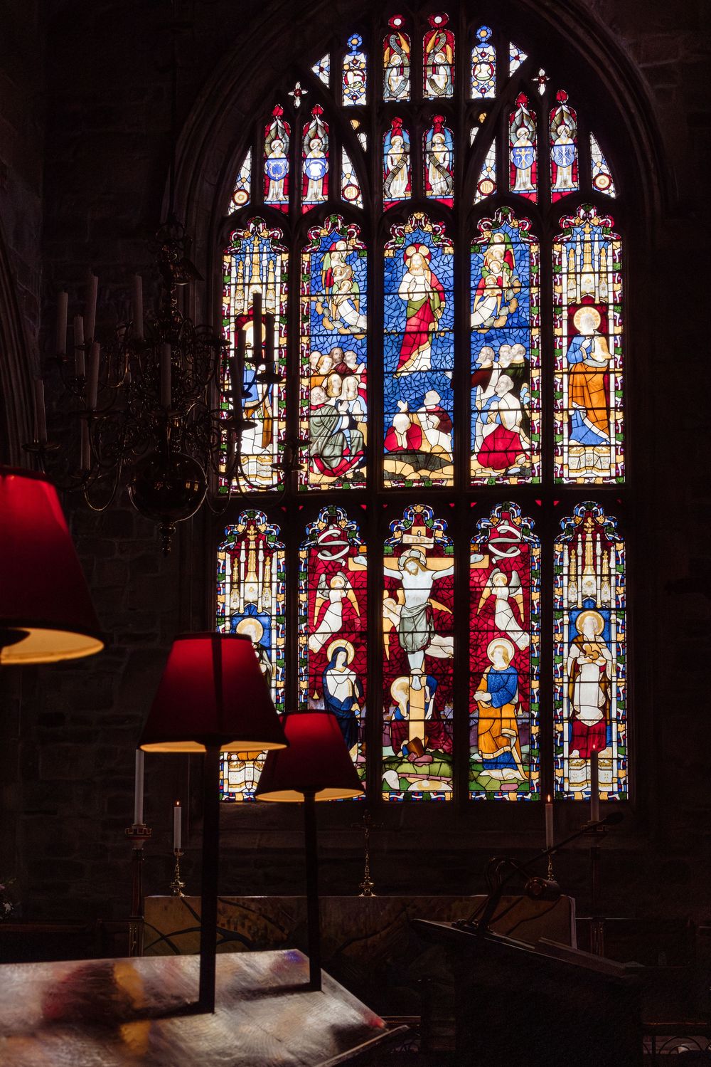 Beautiful stained glass windows in a dark cathedral interior illuminate colorful biblical scenes and religious figures.
