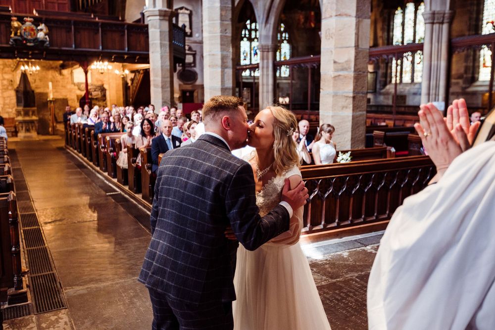 Wedding guests stand and applaud during a joyous celebration in a traditional church setting.