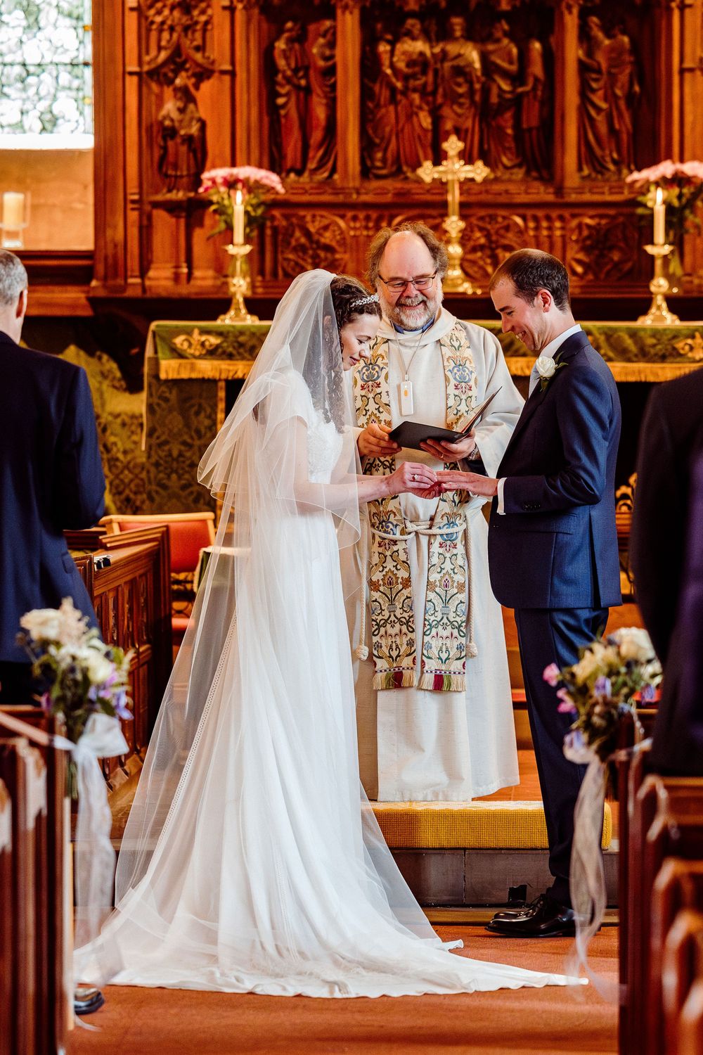 Wedding ceremony taking place in an ornate church with wooden pews and stained glass windows in warm lighting.