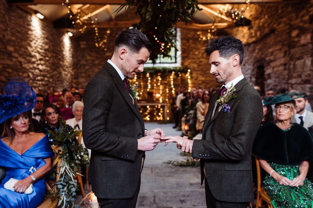 Wedding couple exchanges rings during romantic candlelit ceremony in rustic stone venue.