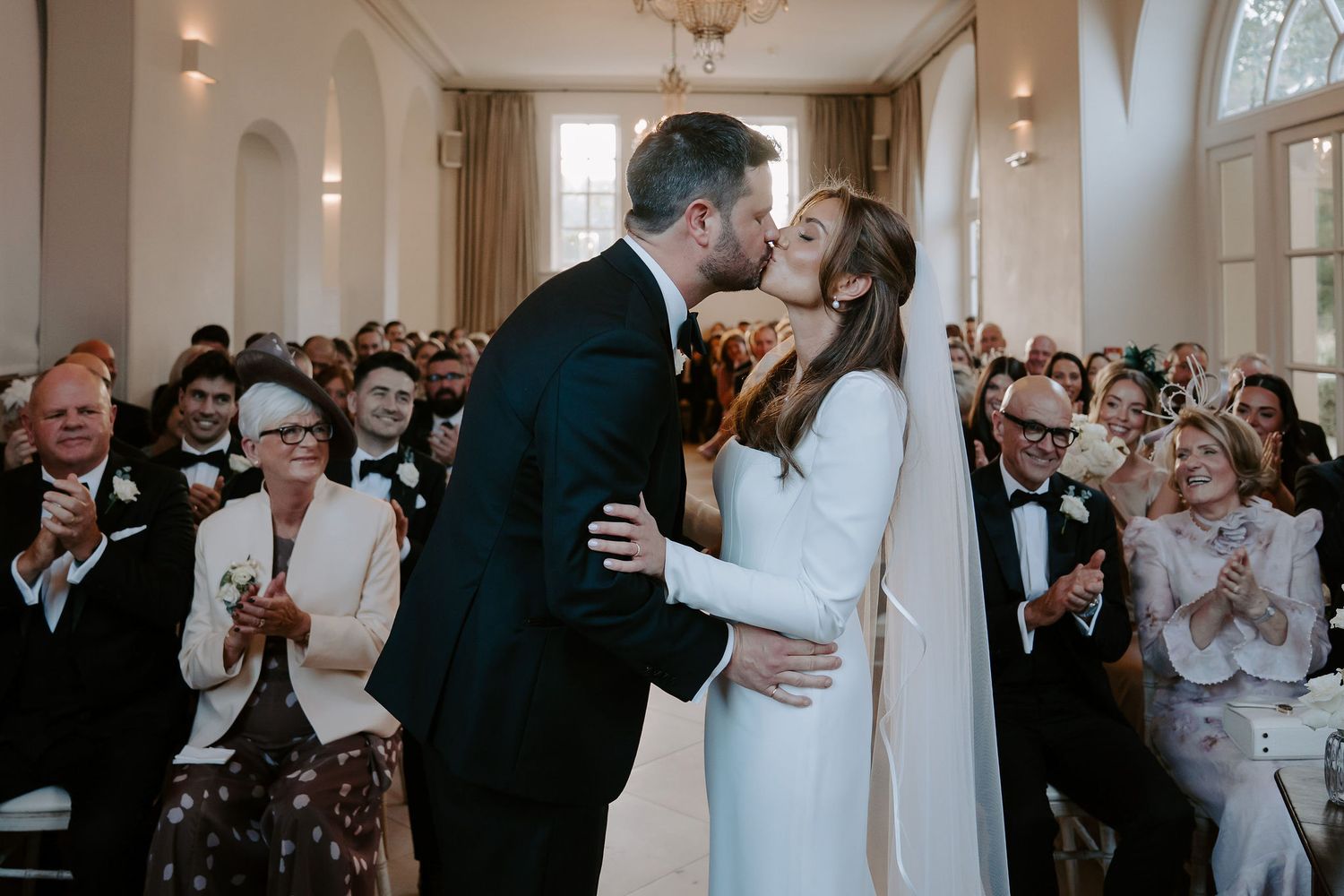 bride and groom sharing their first kiss at the alter surrounded by their guests cheering and clapping at Iscoyd park