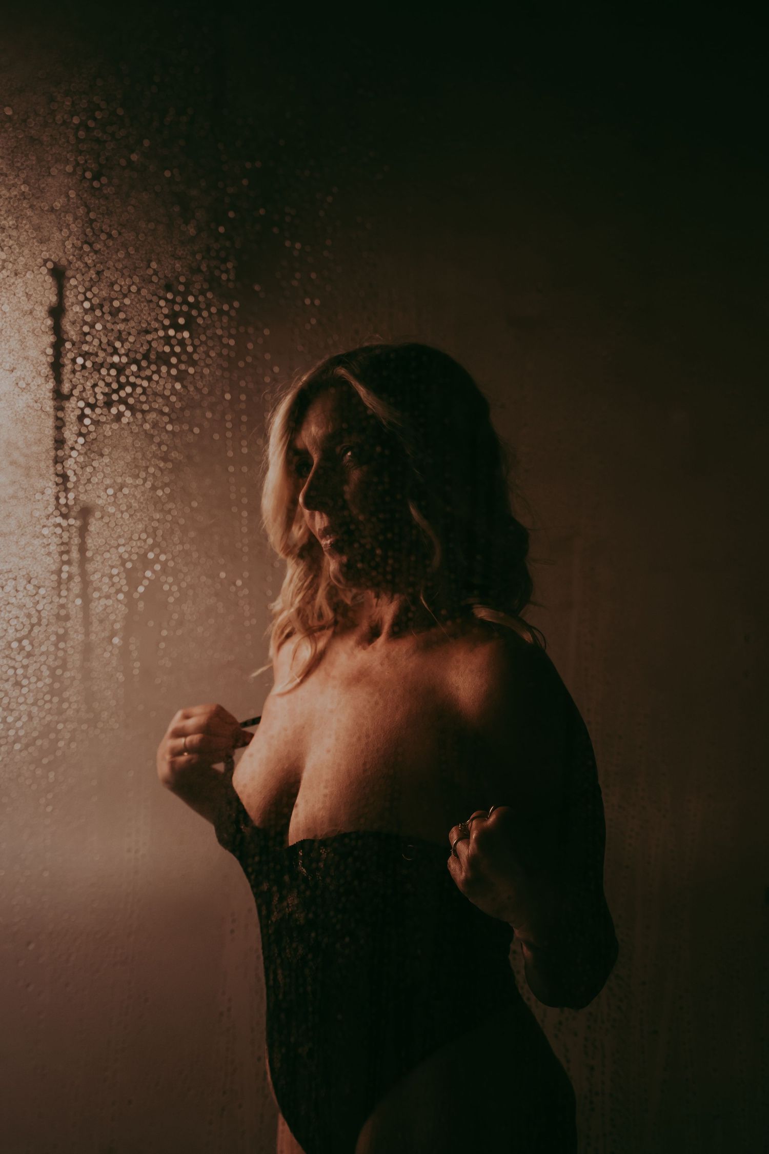 Vrouw met blonde haren en een zwarte lingerie body aan heeft met druppels op de voorgrond