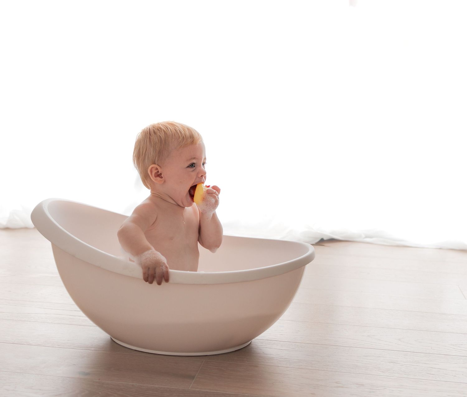 Baby wearing a white dress and sparkly party hat sits against white backdrop during first birthday photoshoot.Photography in Buckinghamshire