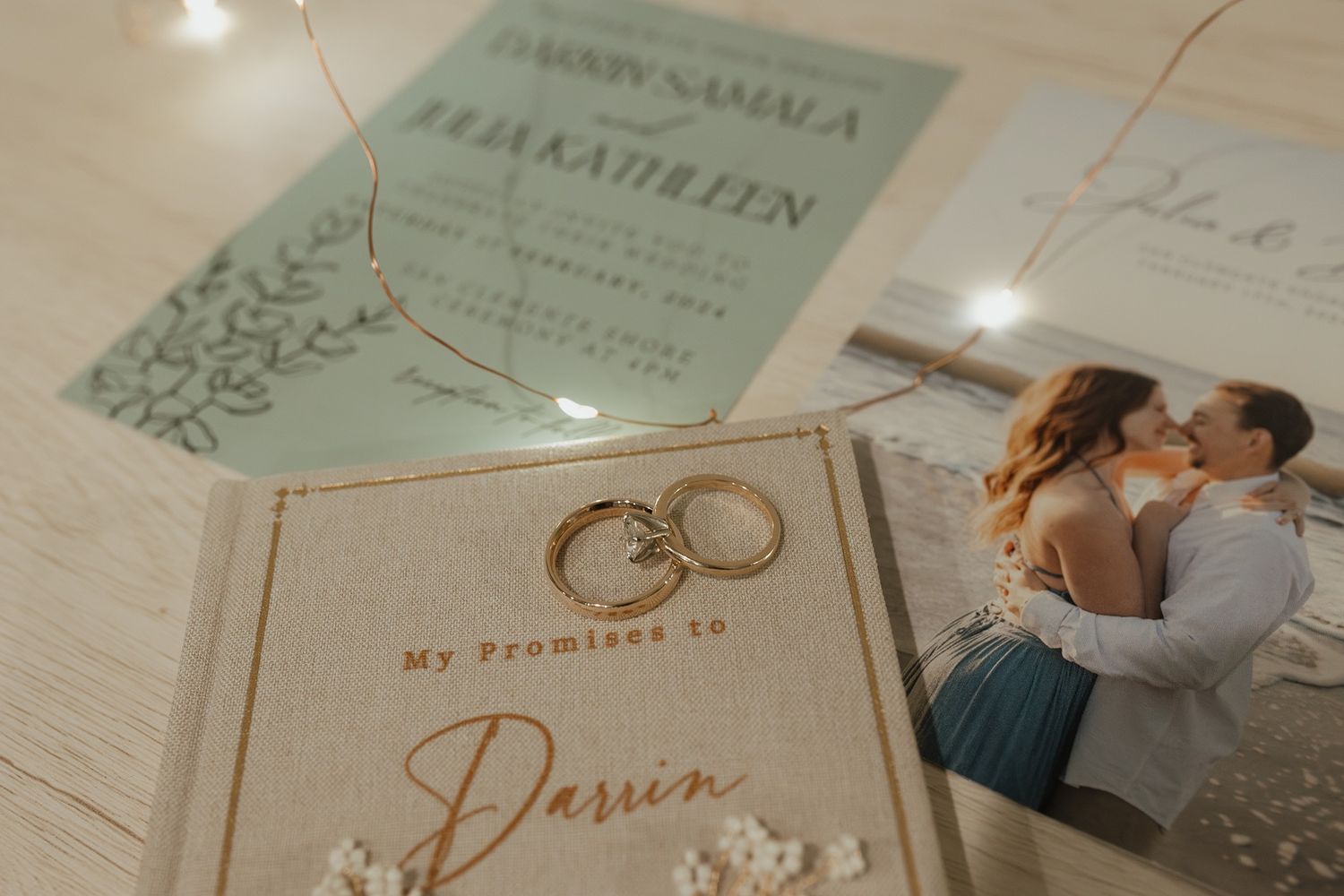A collection of wedding stationery and decor items arranged on a light wooden surface with a soft, muted sage green color scheme.