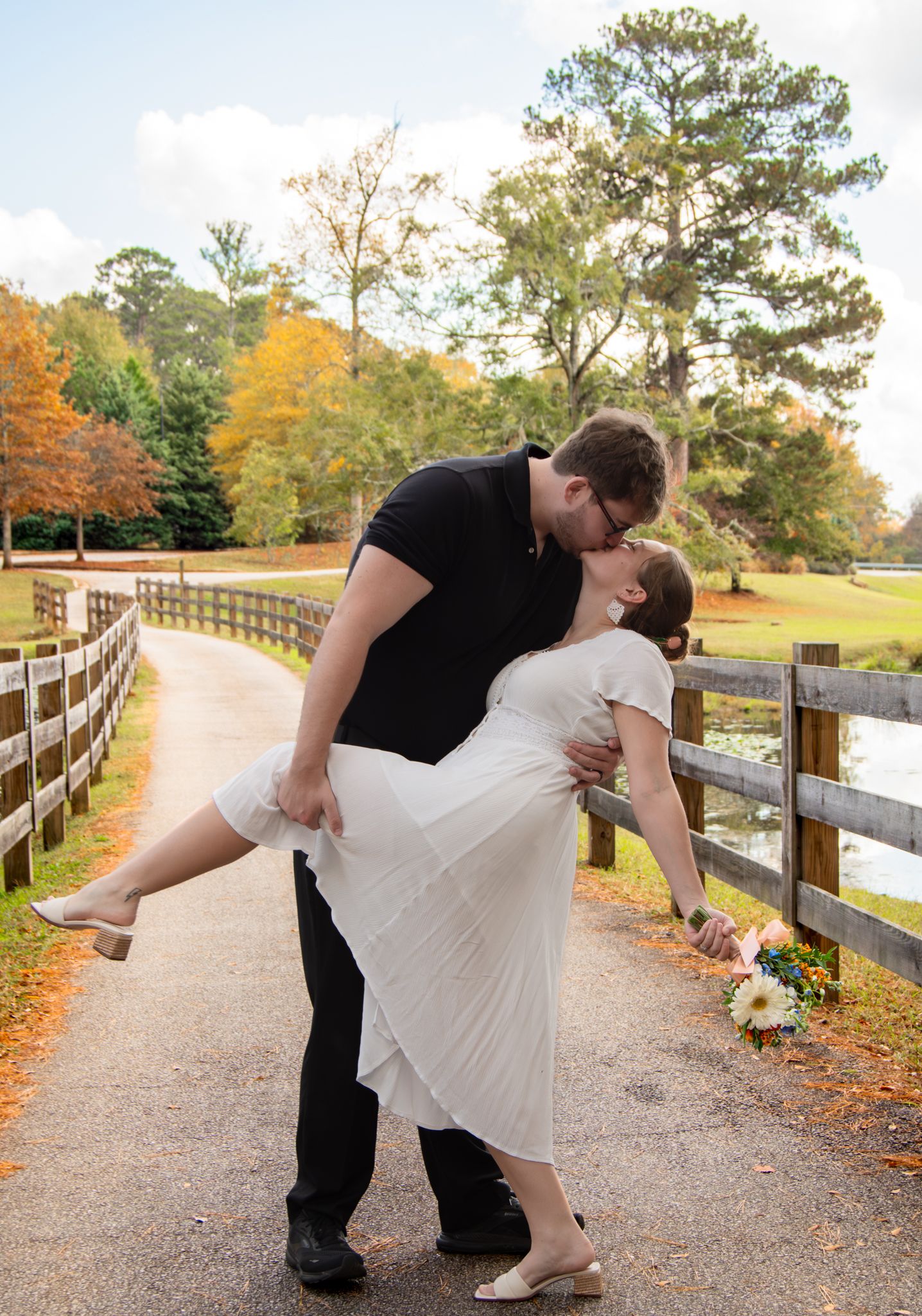 A couple performs romantic dip poses in a series of photos along a scenic autumn path with wooden fencing.
