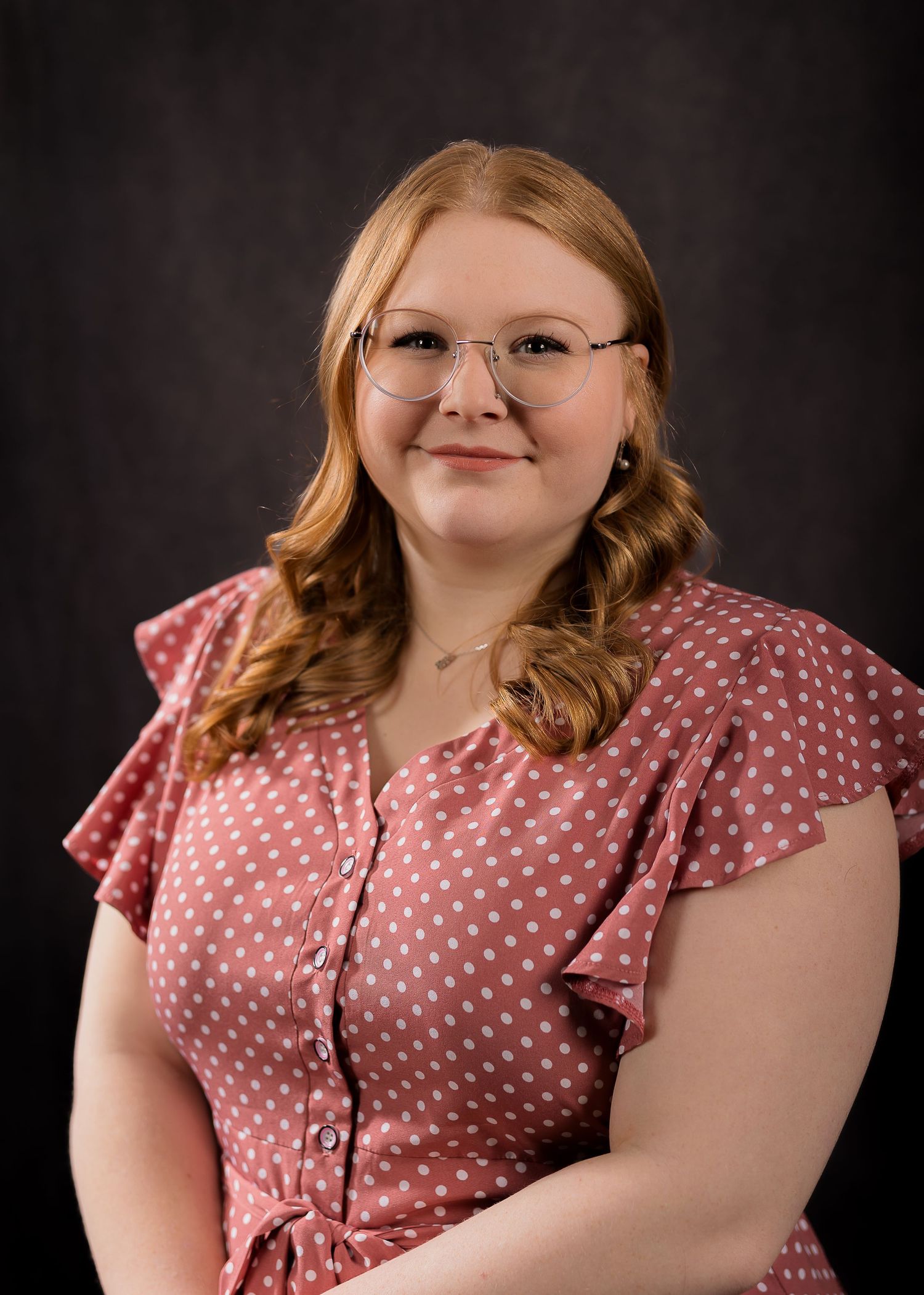 A person wearing a pink polka dot dress poses against a dark background in a series of headshots.
