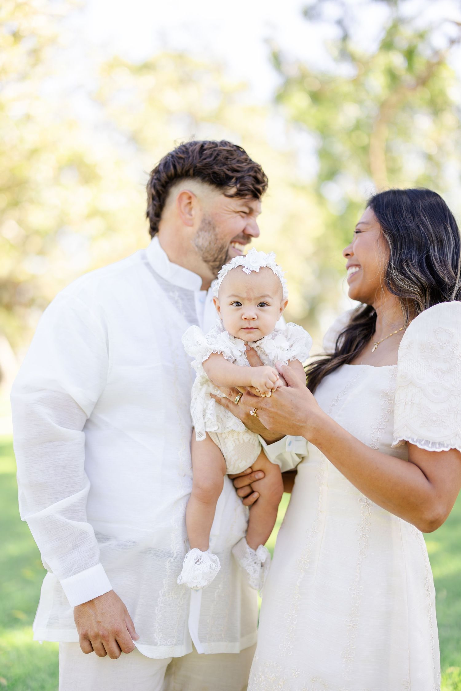 A happy family shares a joyful moment together outdoors on a sunny day wearing coordinated white outfits.