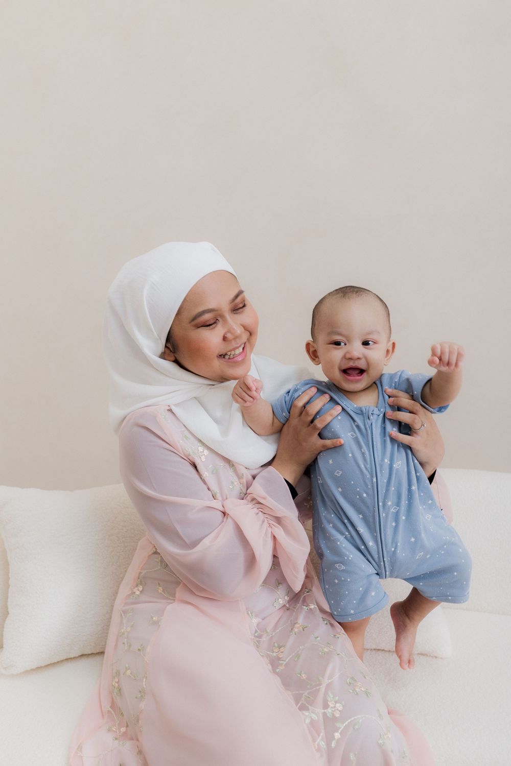 A parent and baby share joyful moments together while sitting on a white couch in matching pink and blue outfits.