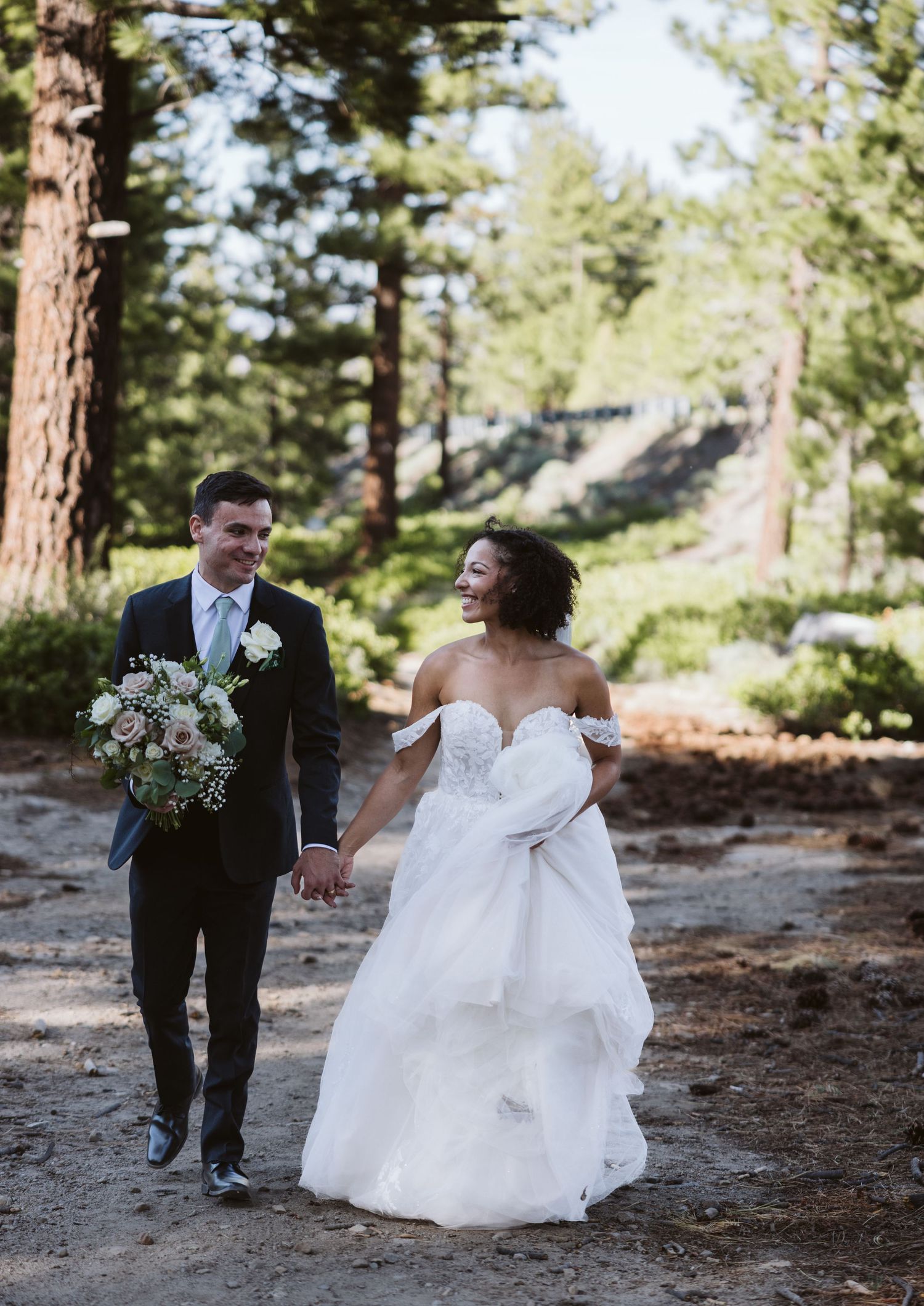 Wedding couple walking through a sunlit pine forest in formal attire.
