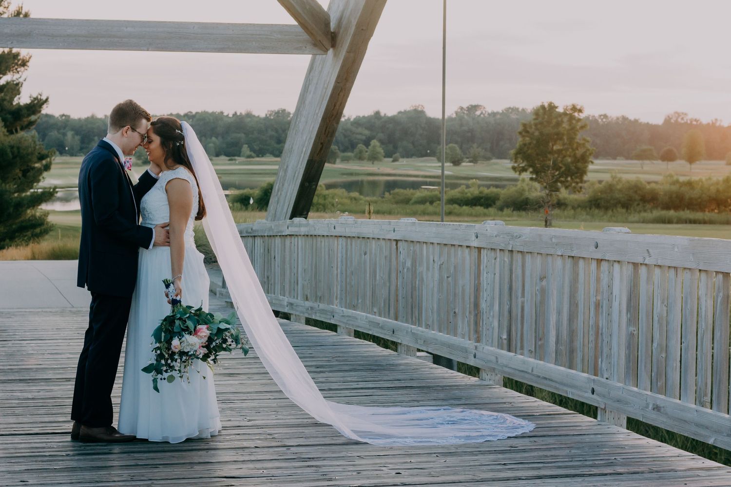 Bride and groom sharing romantic moment on wooden bridge at sunset.