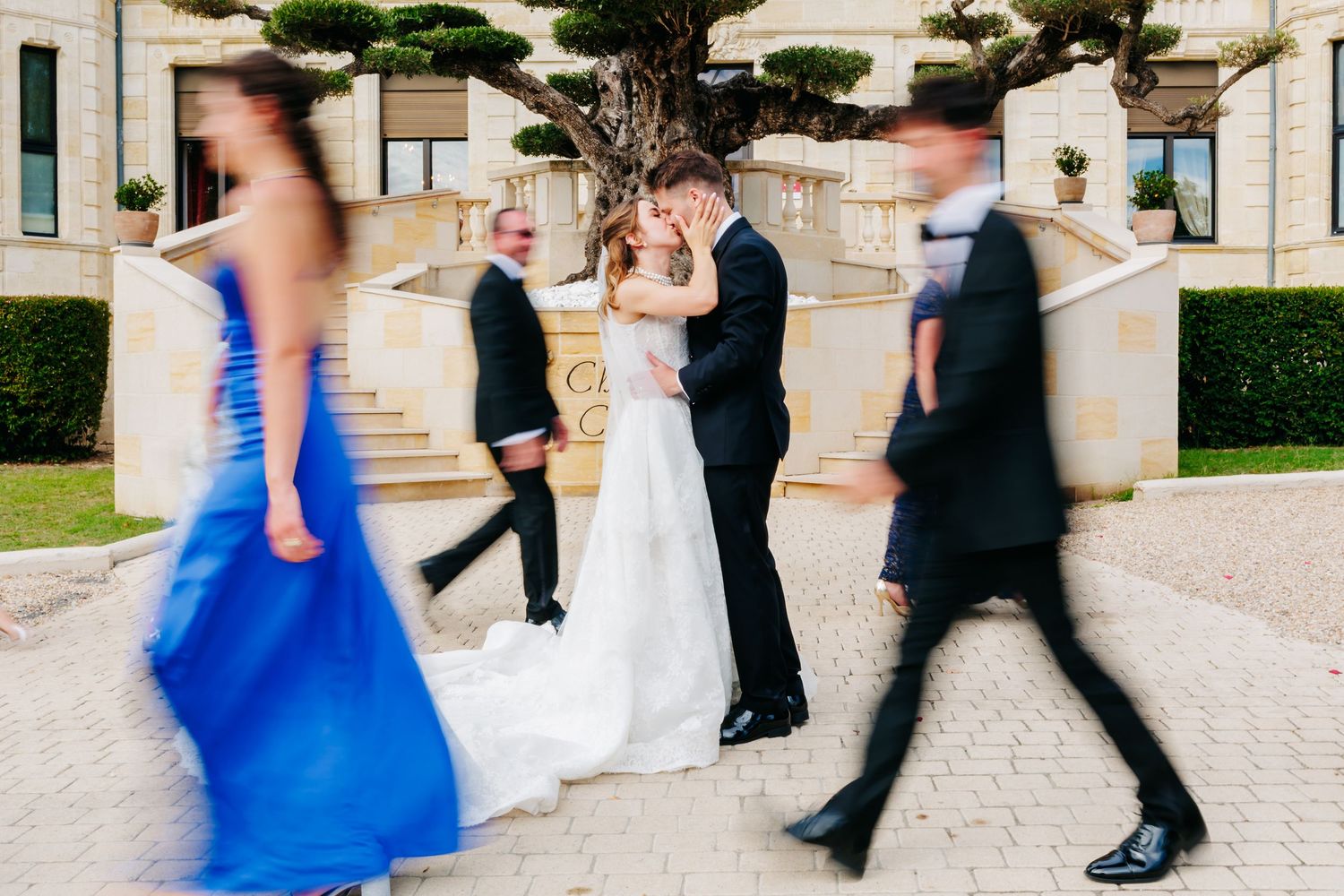 A couple in formal attire dances and celebrates joyfully on a wooded forest path surrounded by greenery.