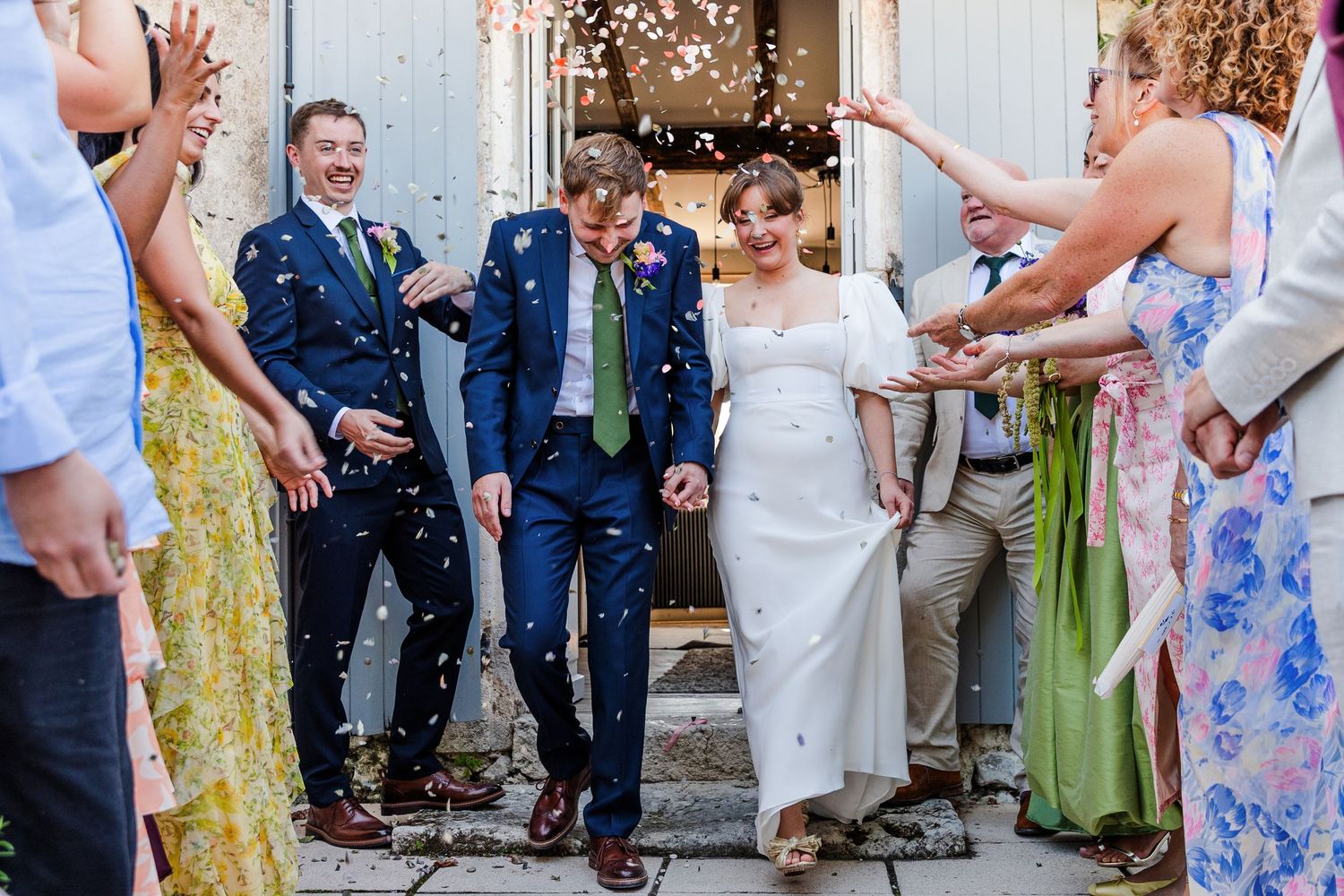 A couple in formal attire dances and celebrates joyfully on a wooded forest path surrounded by greenery.