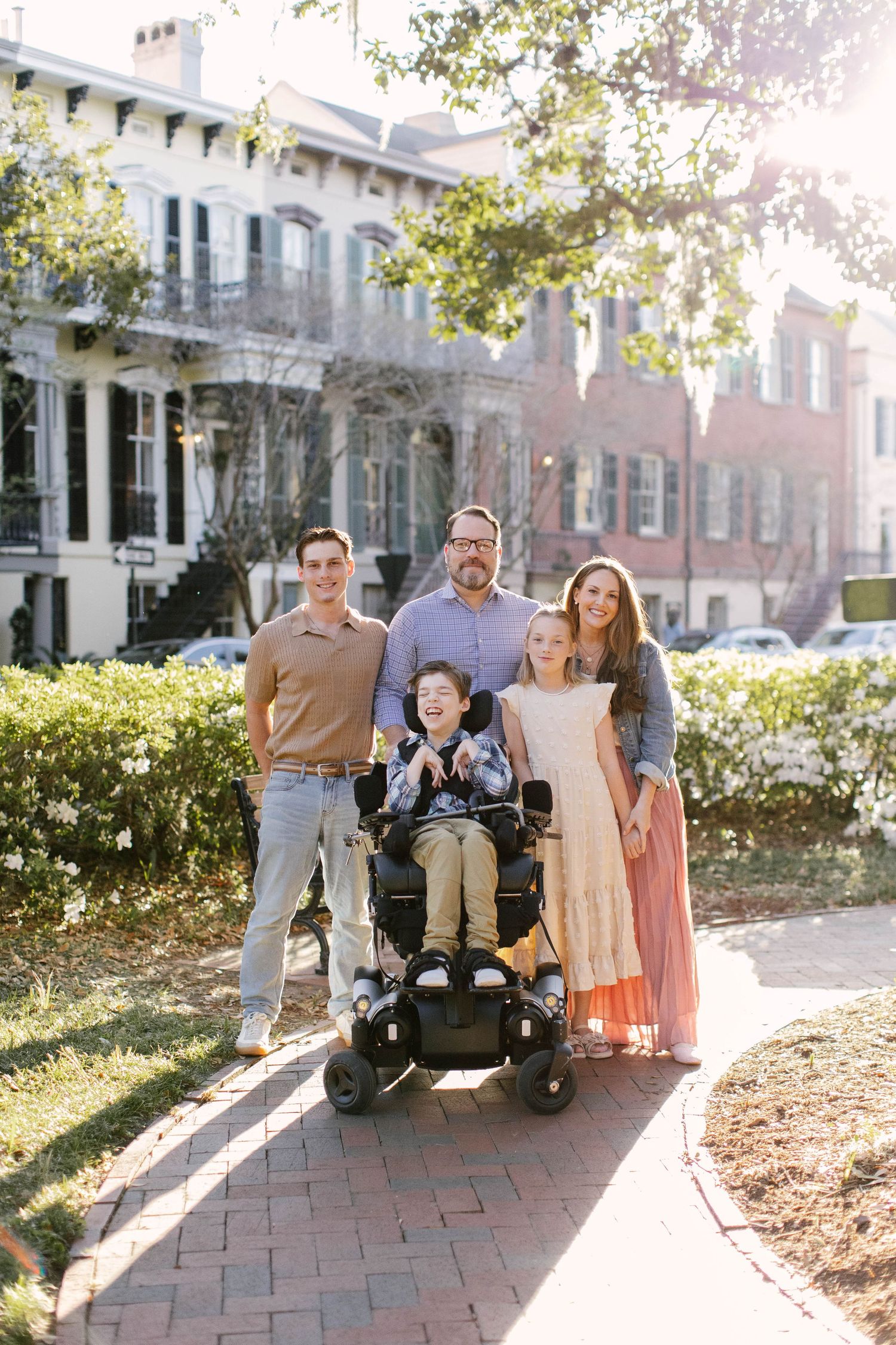 A family poses together on a brick pathway outside a historic building on a sunny autumn day.
