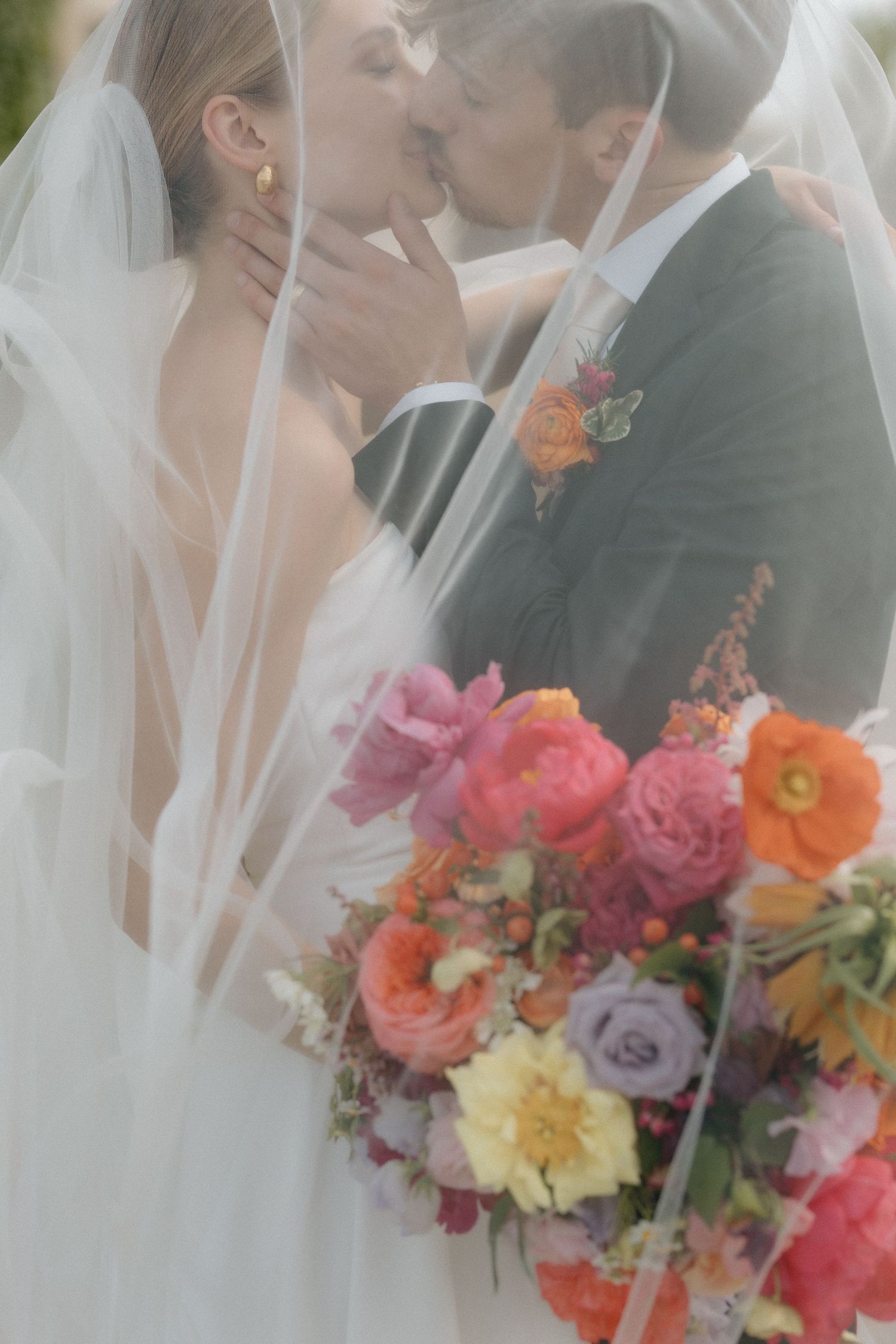 A wedding couple embraces near vibrant coral and pink floral arrangements during an intimate ceremony moment.