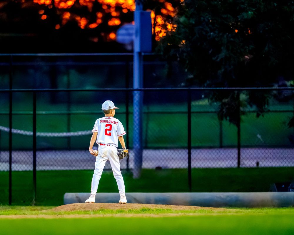 Youth baseball outfielder standing ready in the field at sunset, SportsFox Photography.