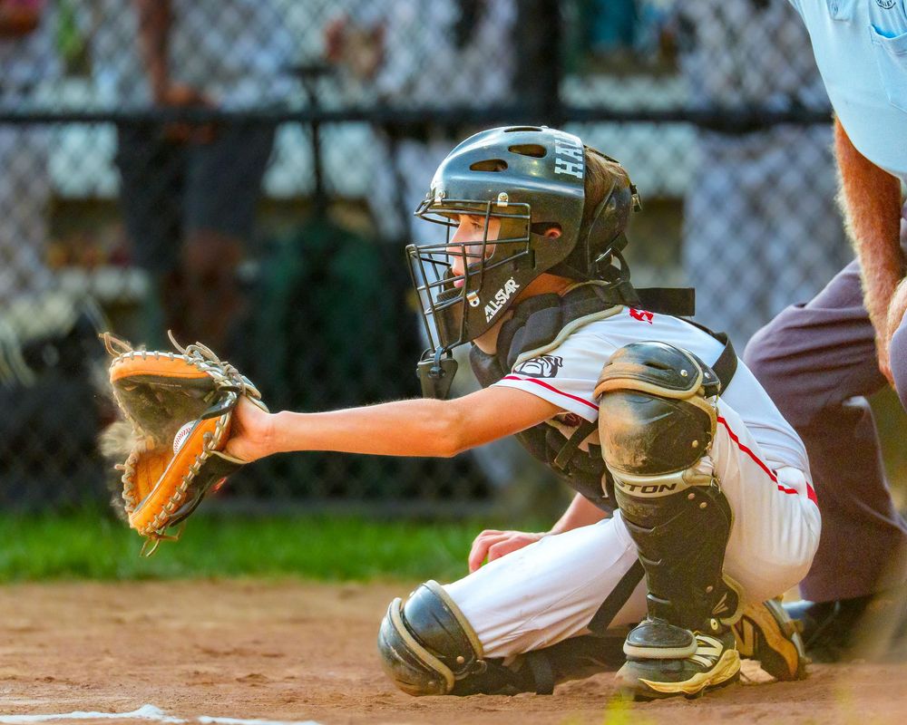 Youth baseball catcher in full gear ready to receive a pitch during a game, action shot behind home plate, SportsFox Photography.