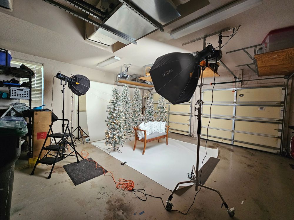 Professional photography studio setup in a garage with lighting equipment, white backdrop and decorated Christmas tree.