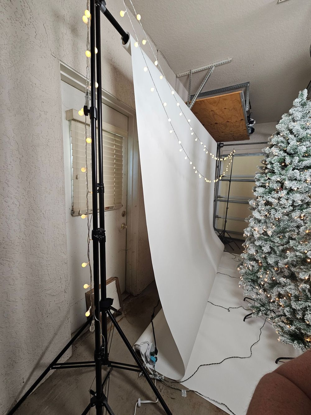 Photography studio setup with white backdrop, lighting equipment, and a decorated Christmas tree in the corner.
