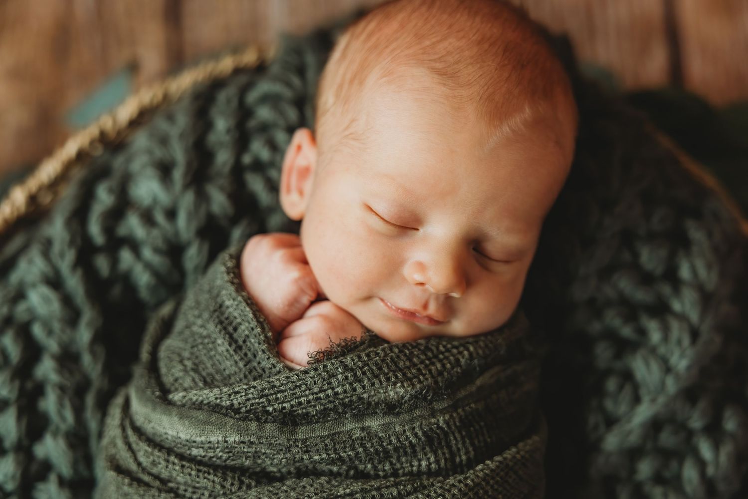 Sleeping newborn wrapped in cozy green knitted blanket during professional photography session.