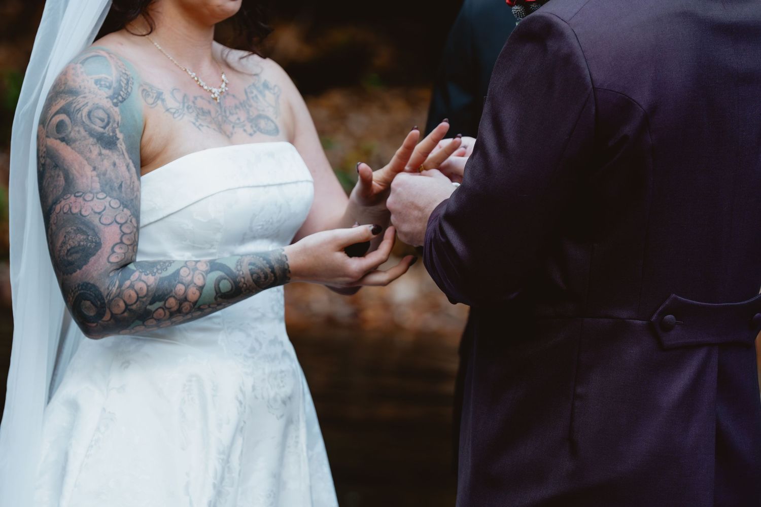 Close-up of hands exchanging wedding rings during an outdoor ceremony with brick wall backdrop.