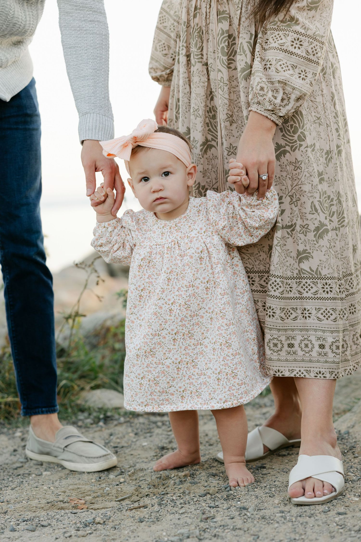 Close-up view of bare feet and floral dresses on sandy ground showing coordinated family fashion details.
