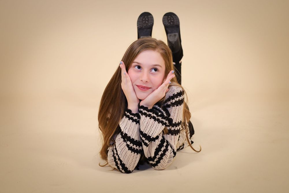 Playful studio portrait lying on floor in striped sweater against beige background.