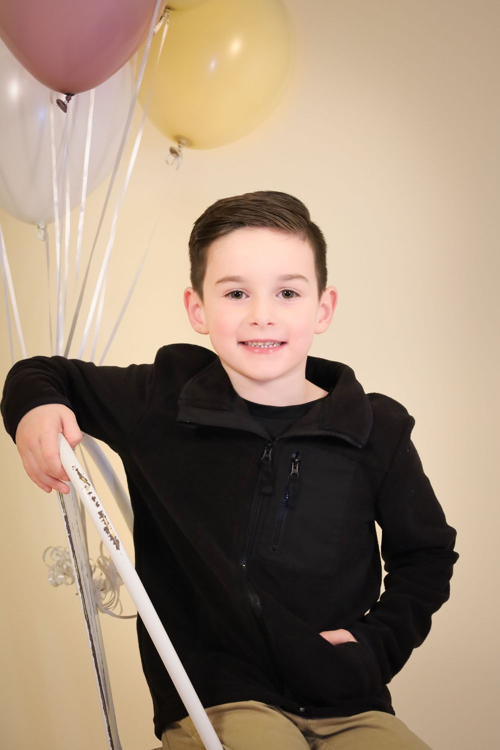 Studio portrait with pastel balloons featuring casual pose on white chair.
