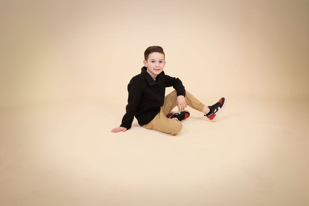Casual studio portrait against beige backdrop showing relaxed seated pose.