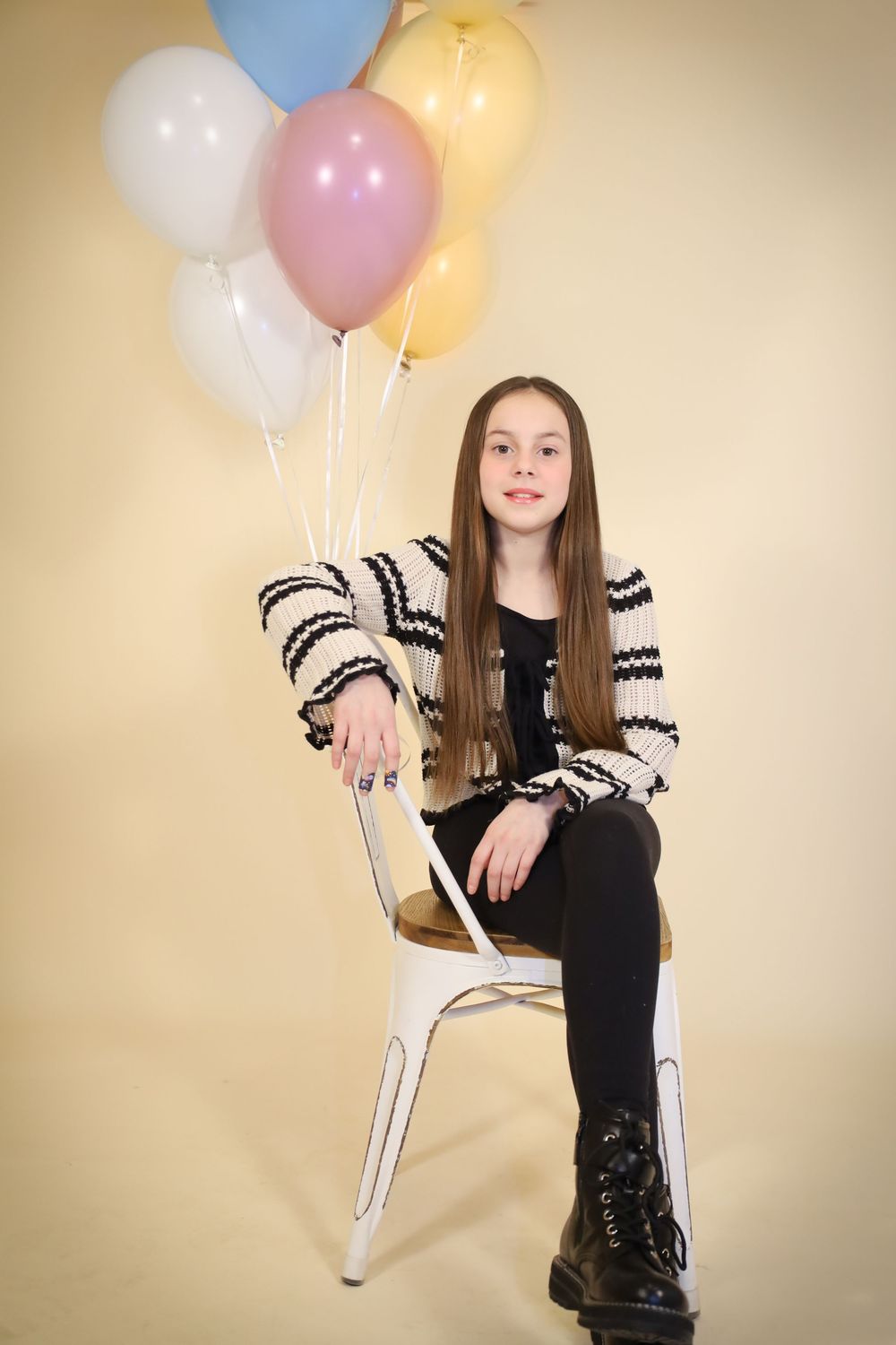 Studio portrait with colorful balloons featuring casual pose on white chair.