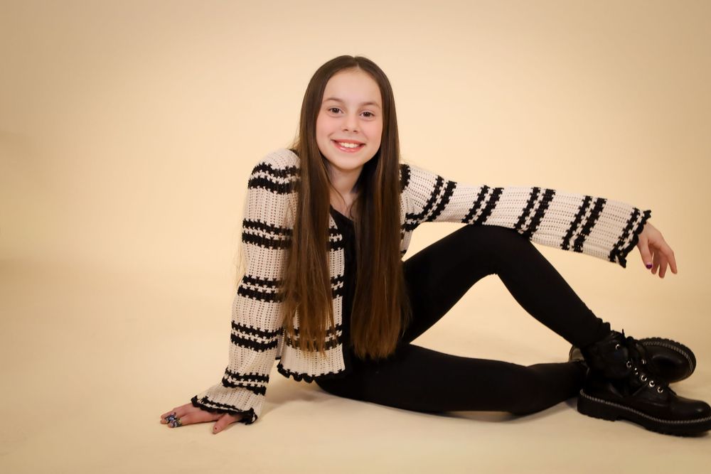 Person in striped sweater and black pants lounging on studio floor against beige backdrop.