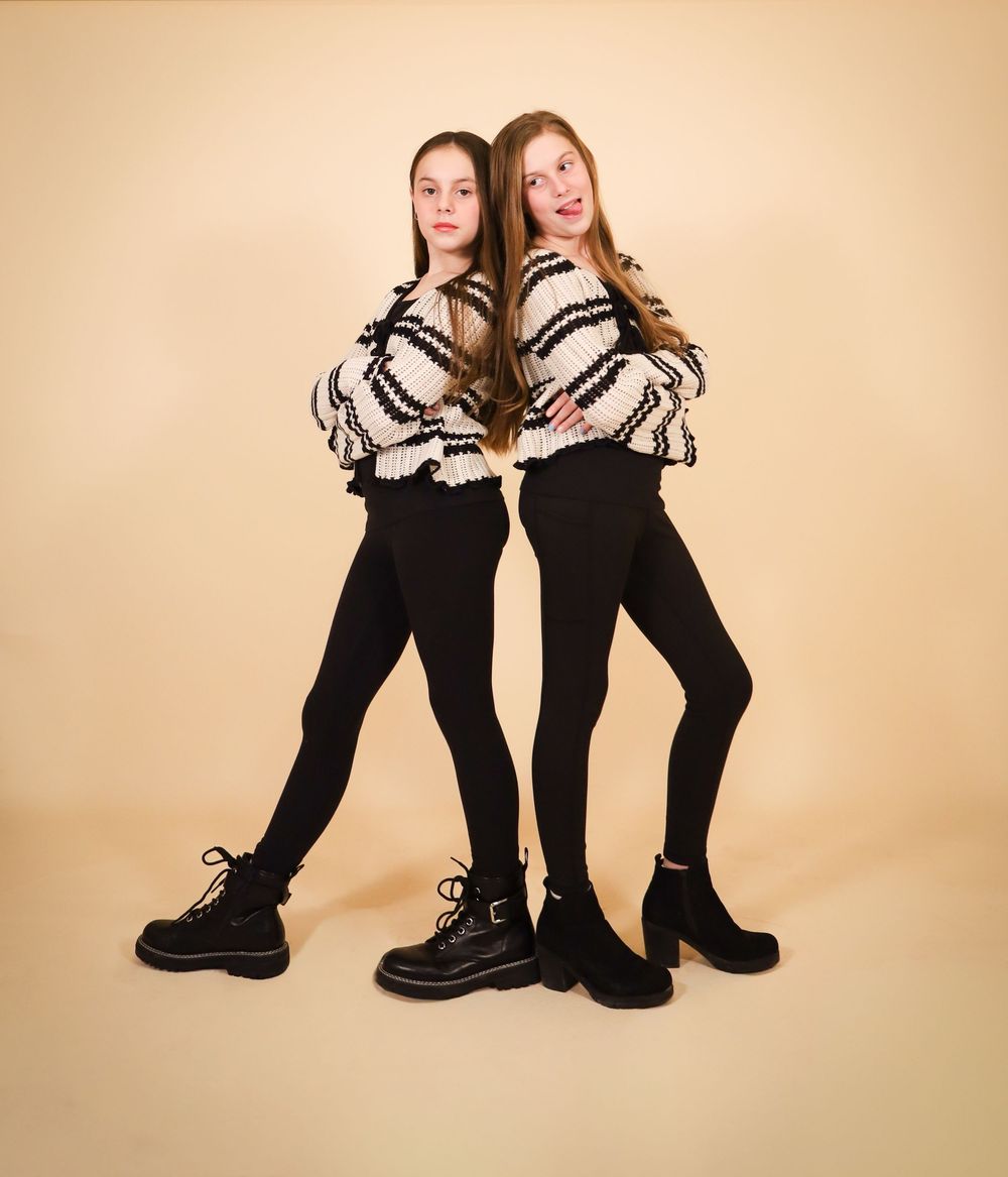 Two people in matching striped sweaters and black pants posing back-to-back in studio setting.