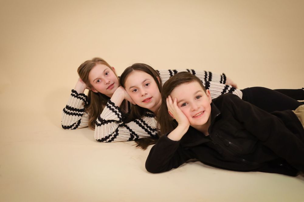 Three people lying on floor wearing coordinated black and white outfits in studio portrait.