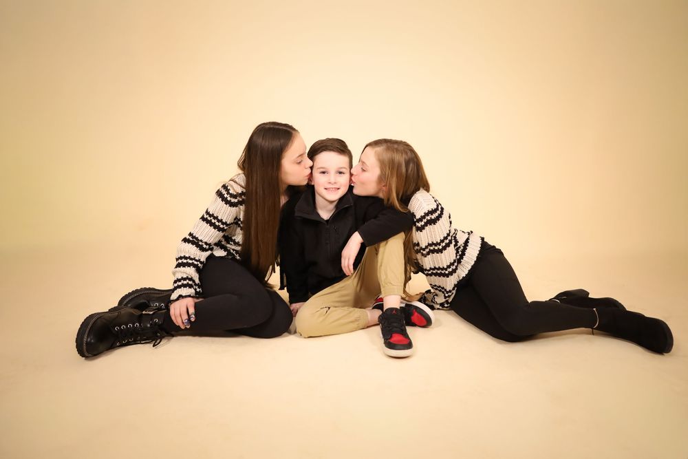 Studio portrait of three people in coordinated outfits sharing an intimate moment on beige background.
