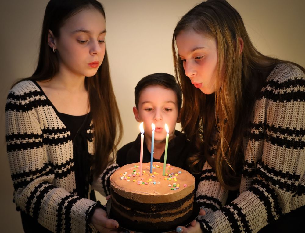 Three people in matching sweaters gathered around birthday cake with glowing candles.
