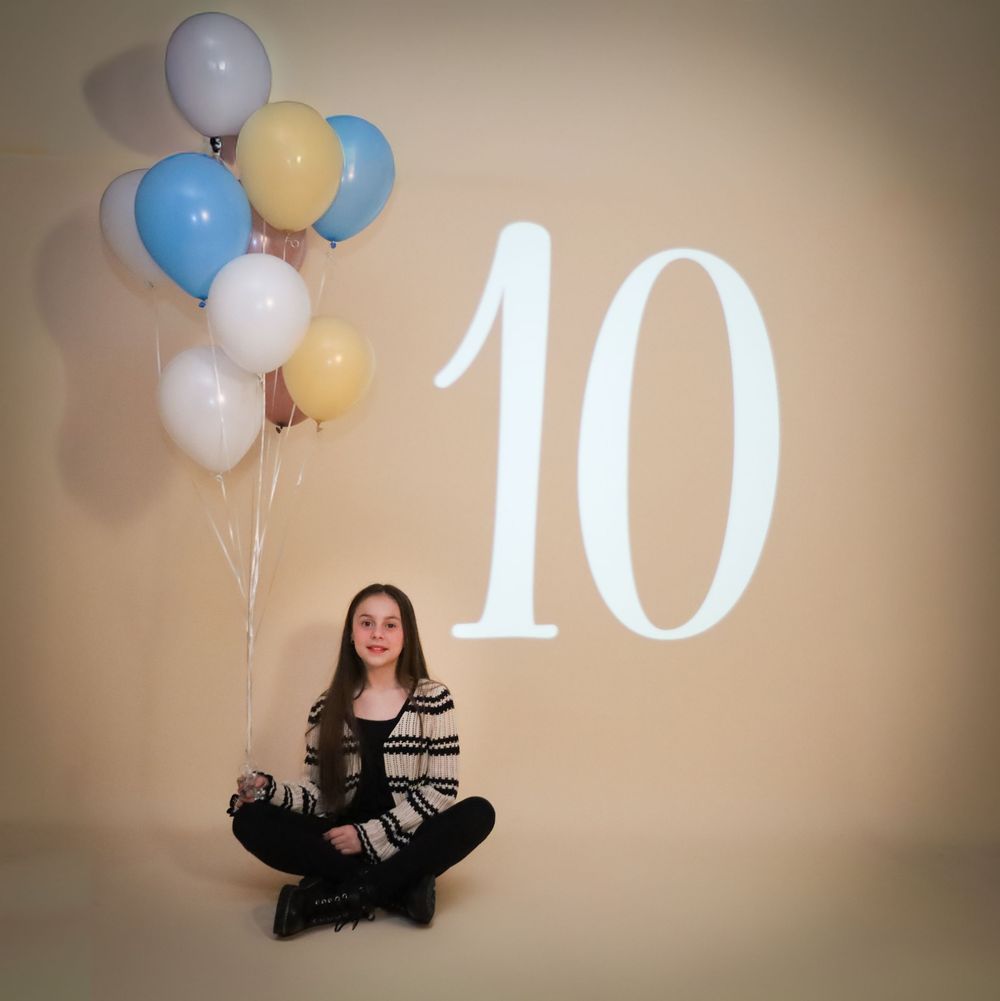 Person in striped sweater sitting cross-legged with colorful balloons next to number 10 on wall.