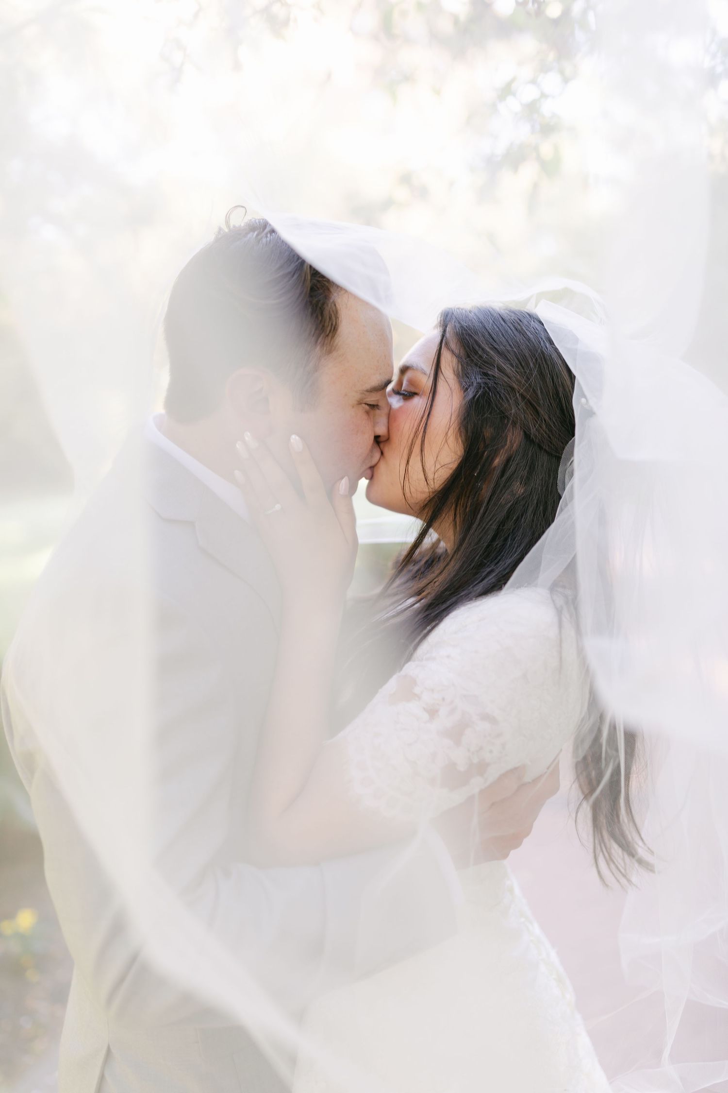 A romantic wedding couple shares tender moments in a garden setting against a stone wall with blooming flowers.