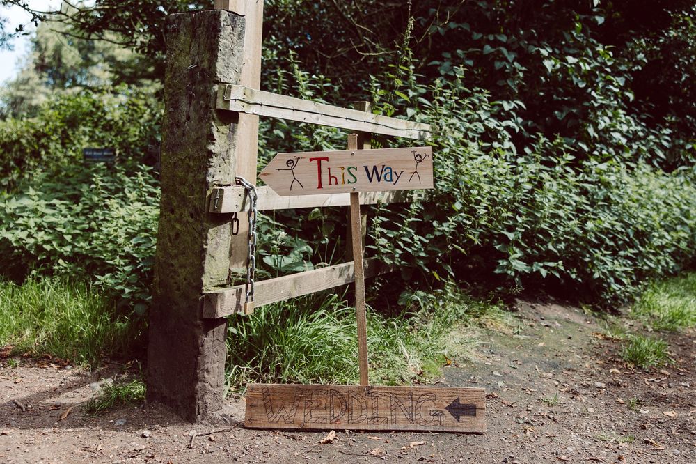 A wooden directional sign reading 'This Way' points along a wooded trail path through green foliage.