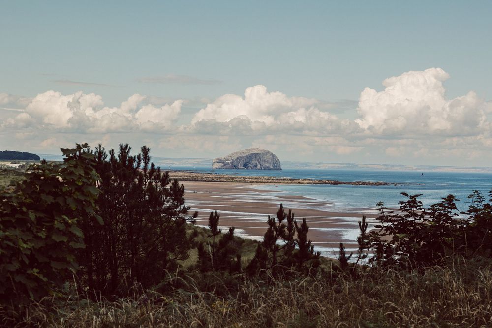 Panoramic coastal landscape with rolling hills and dramatic cliffs overlooking a vast ocean under cloudy skies.