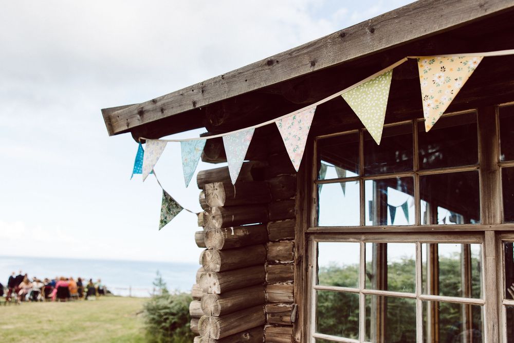 Rustic wooden shelter decorated with triangular bunting flags overlooking a scenic beach view.