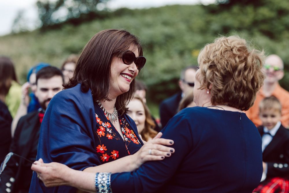 Two people share an emotional embrace outdoors while surrounded by a crowd at a gathering.