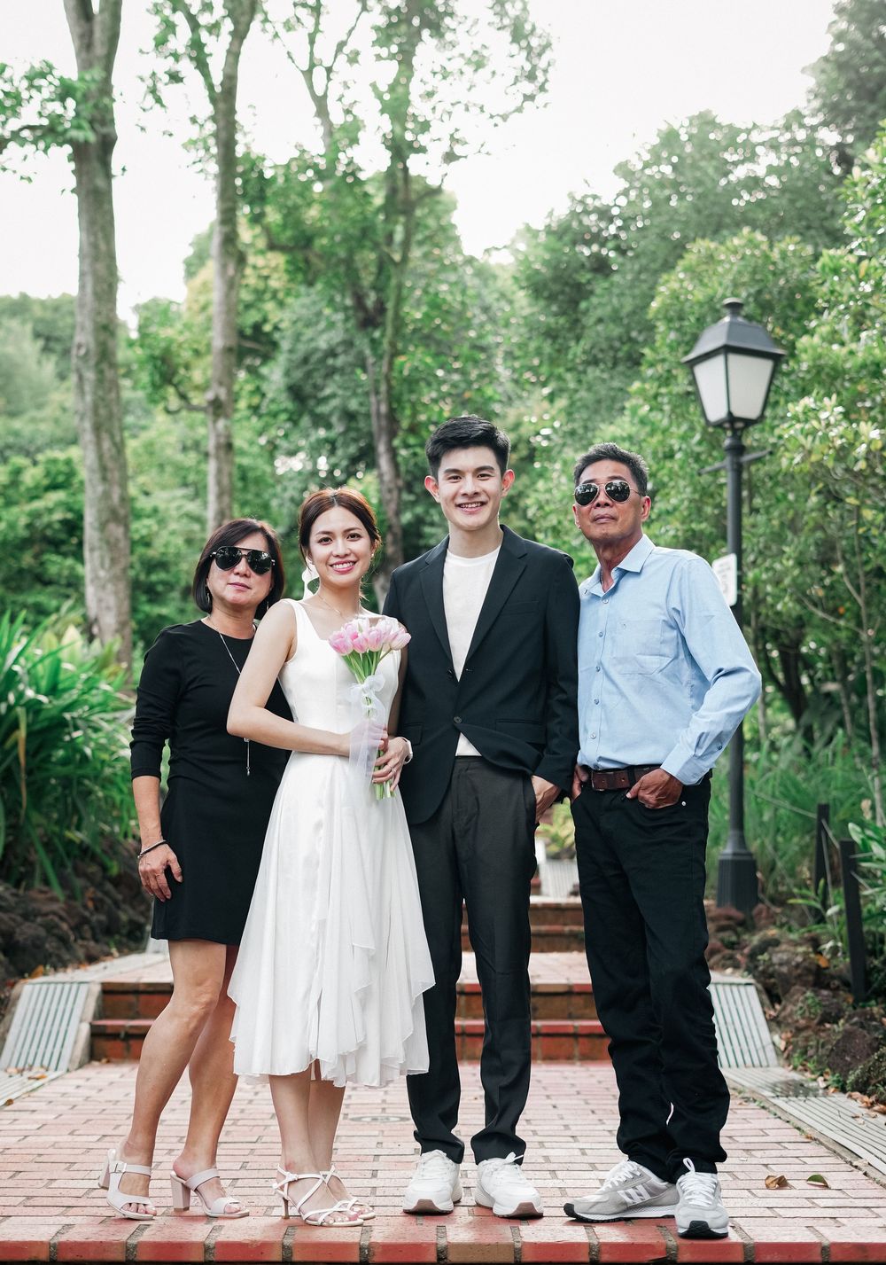 Group photo outdoors in a garden setting with brick path and lamp post against lush green foliage background.