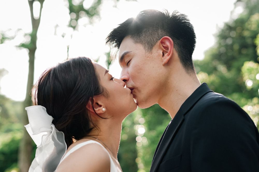 Newlyweds share a romantic kiss in a garden setting.