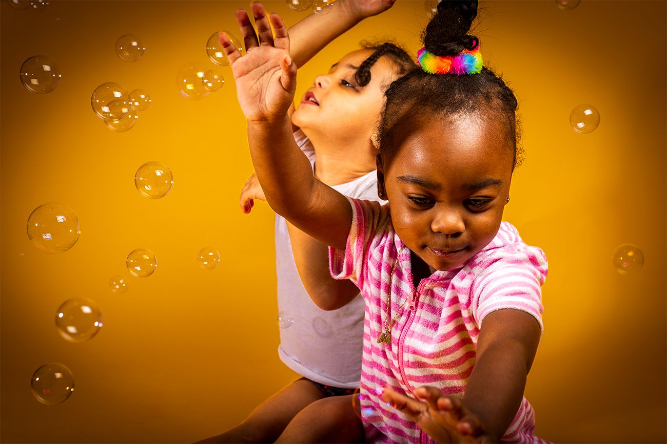 Child playing with bubbles against vibrant yellow background with pure joy.