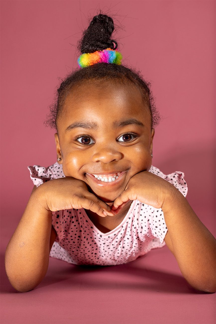 Portrait against pink background wearing colorful hair accessories and polka dot dress.