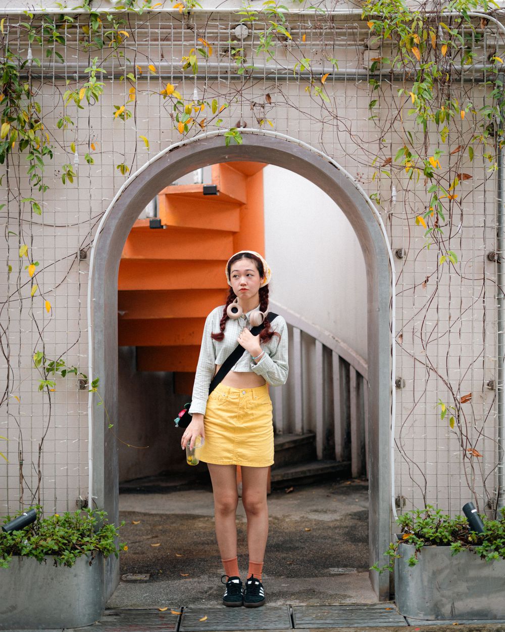 A yellow skirt and white sweater outfit posed in a stone archway with orange stairs and climbing vines.
