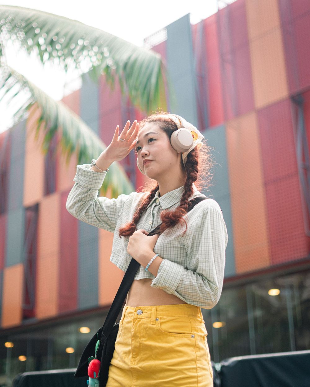 Street style fashion with yellow skirt and headphones against colorful urban backdrop.