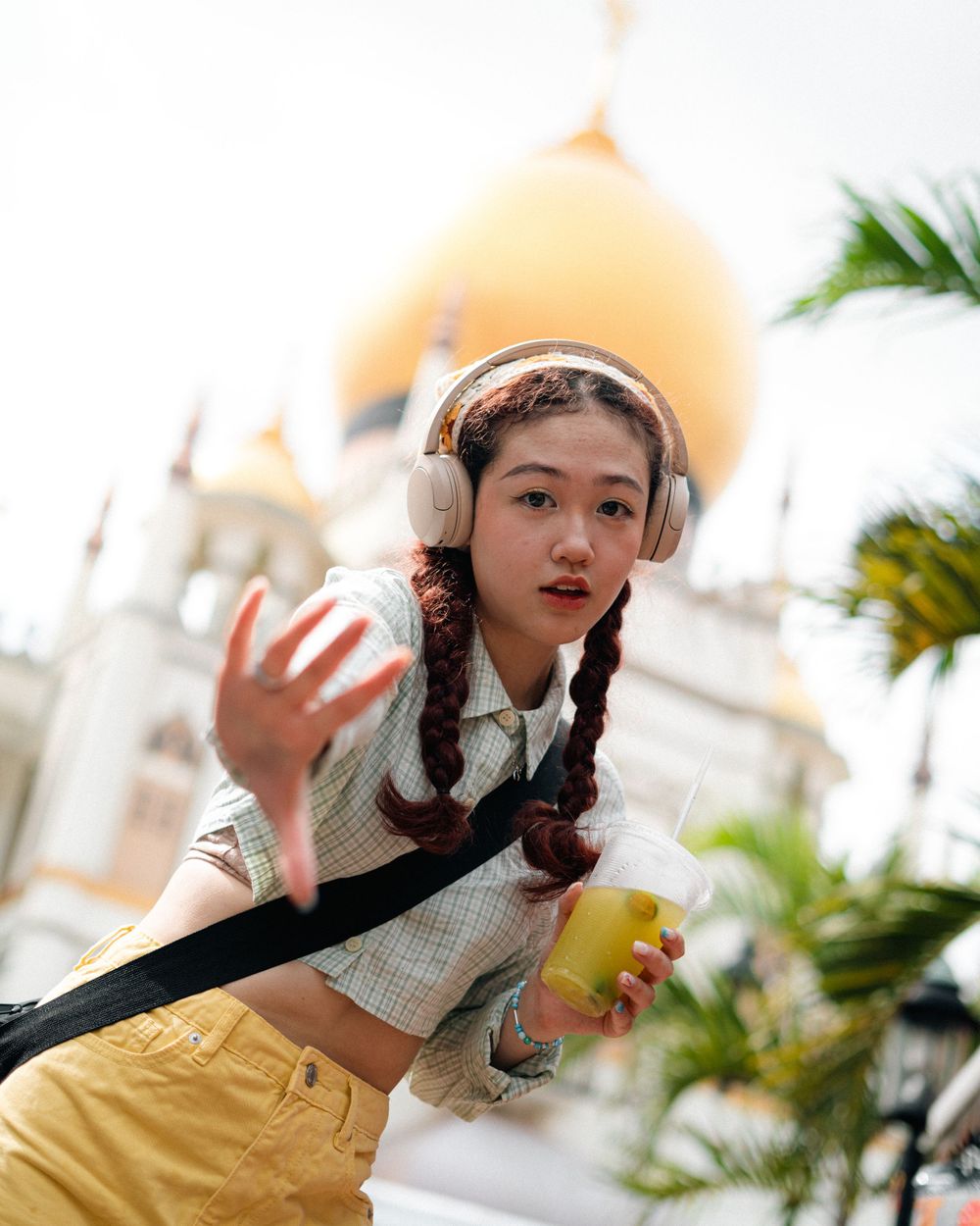Casual street style with yellow drink against mosque architecture background.