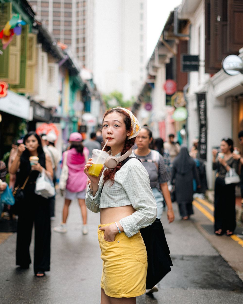 A candid street photo showing a yellow dress against an urban background with streetside shops and crowds.
