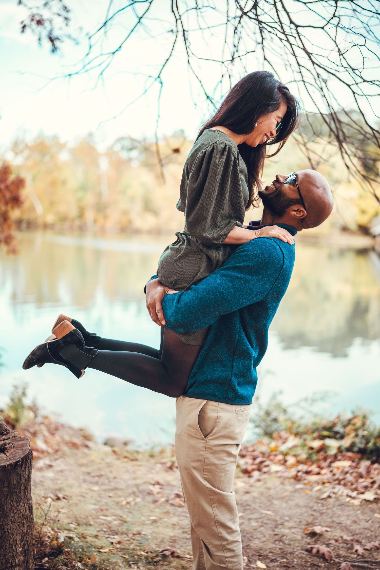 Romantic autumn lakeside scene with a couple embracing by the water as fallen leaves scatter the shore.